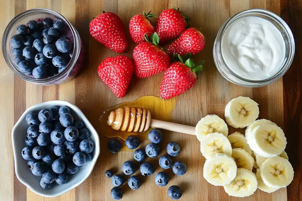 Essential ingredients for a strawberry blueberry smoothie, including strawberries, blueberries, banana, yogurt, almond milk, and honey on a wooden surface.